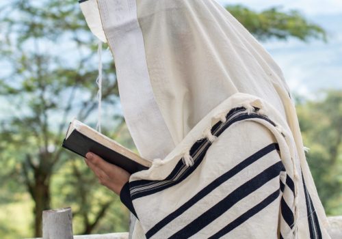 Jew praying and reading the siddur while raising his right arm to heaven.
